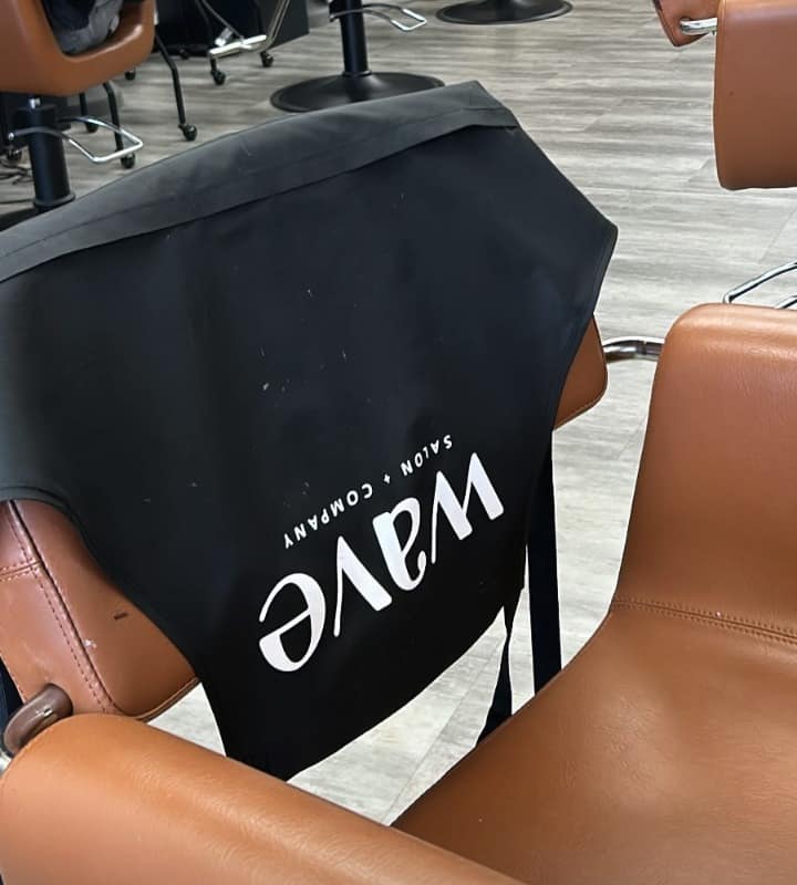 Wave Salon + Company branded cape draped across a styling chair